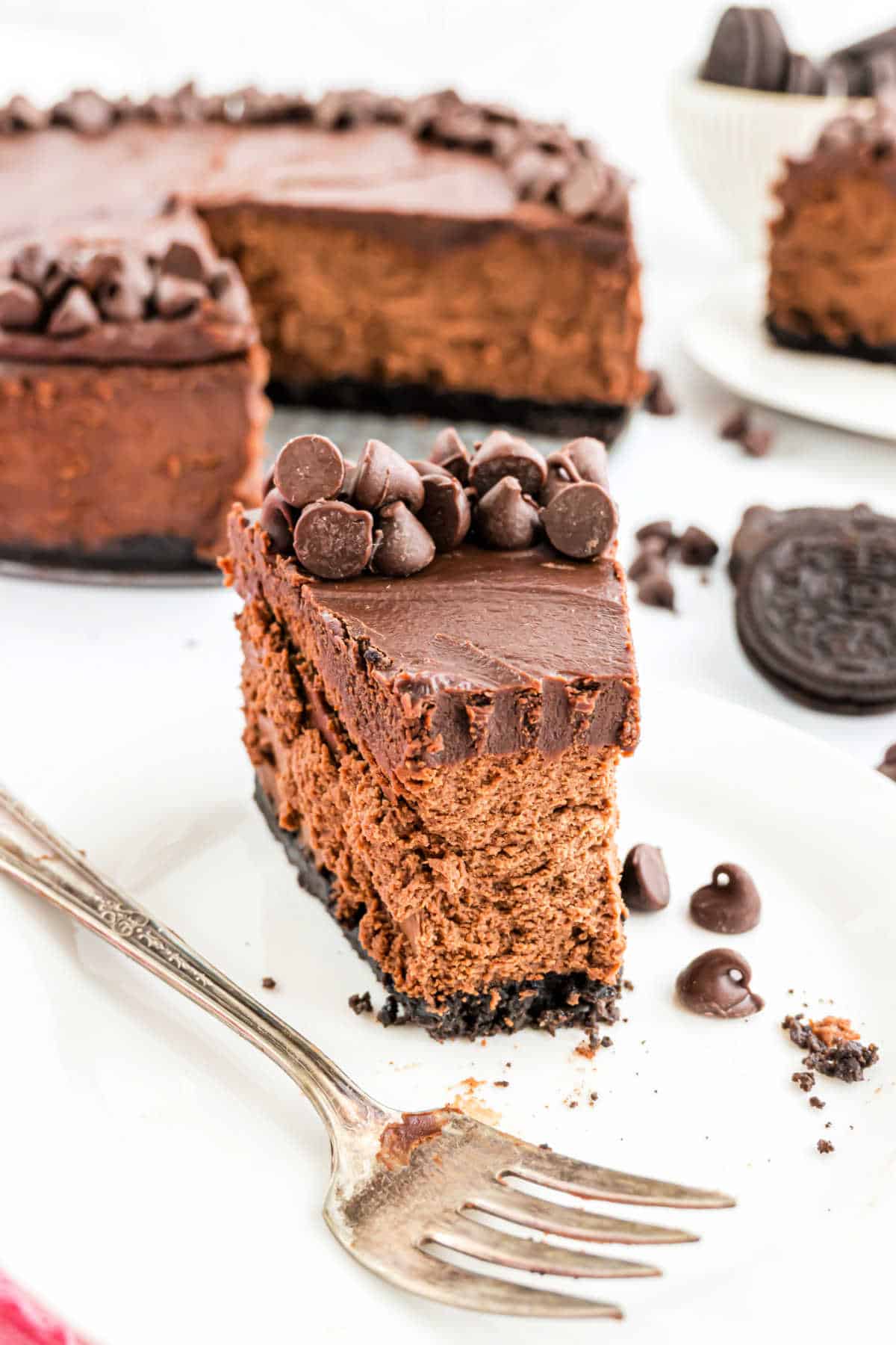 A decadent slice of chocolate cheesecake topped with chocolate chips sits on a plate, a fork resting beside it.