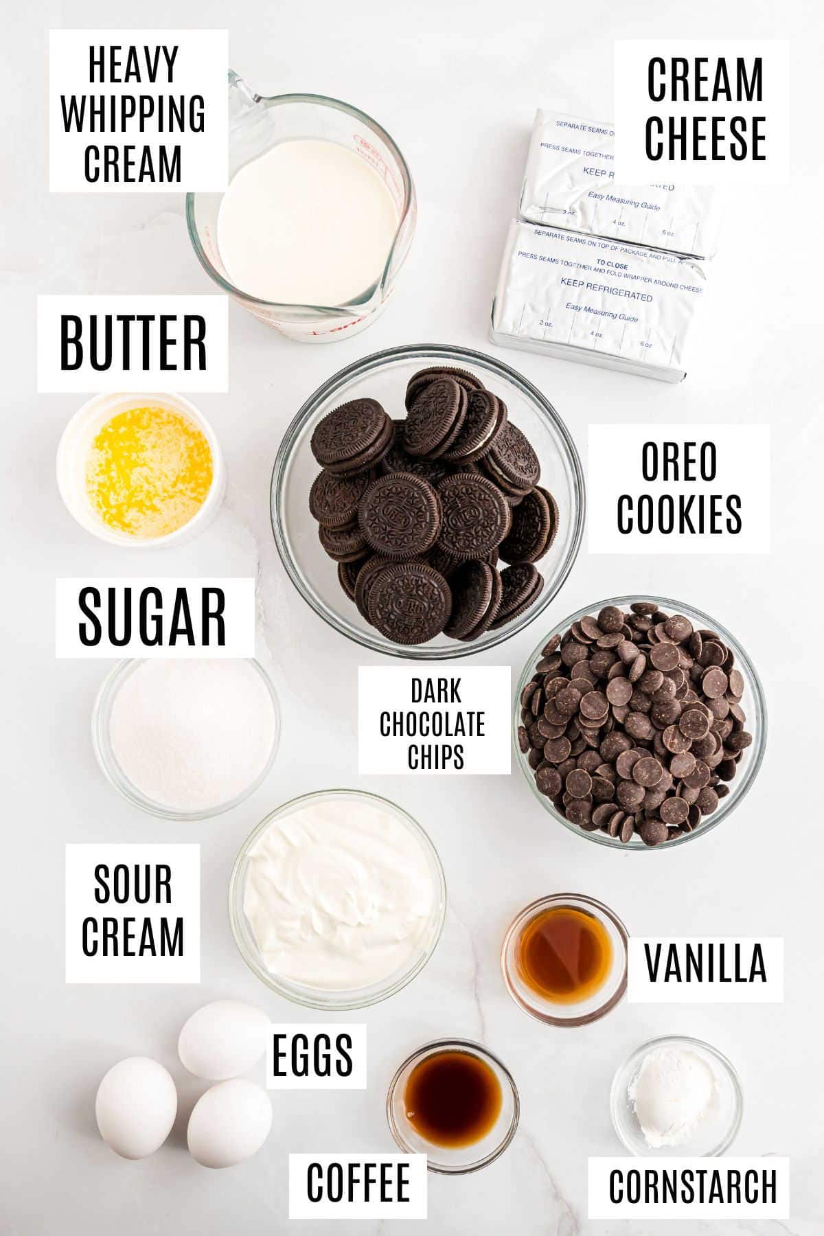Top-down view of labeled baking ingredients for a chocolate cheesecake, including Oreo cookies, cream cheese, eggs, sugar, and chocolate chips.