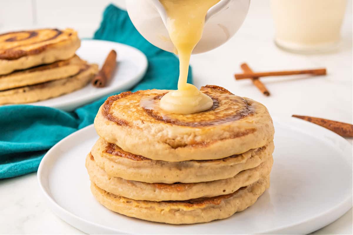 Stack of pancakes with a cream cheese icing being drizzled over the top.