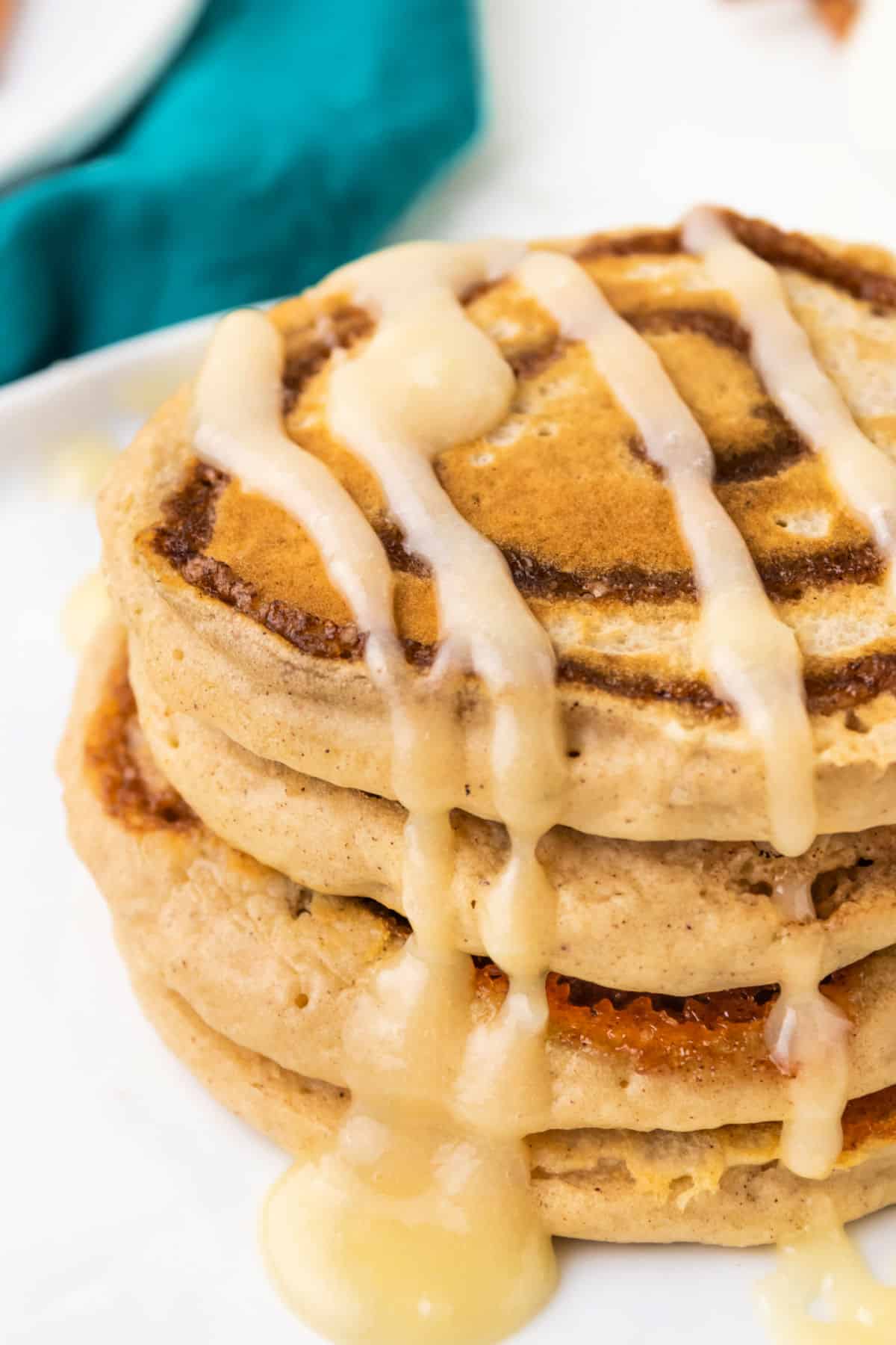 Stack of cinnamon roll pancakes with cream cheese glaze drizzled over the top.