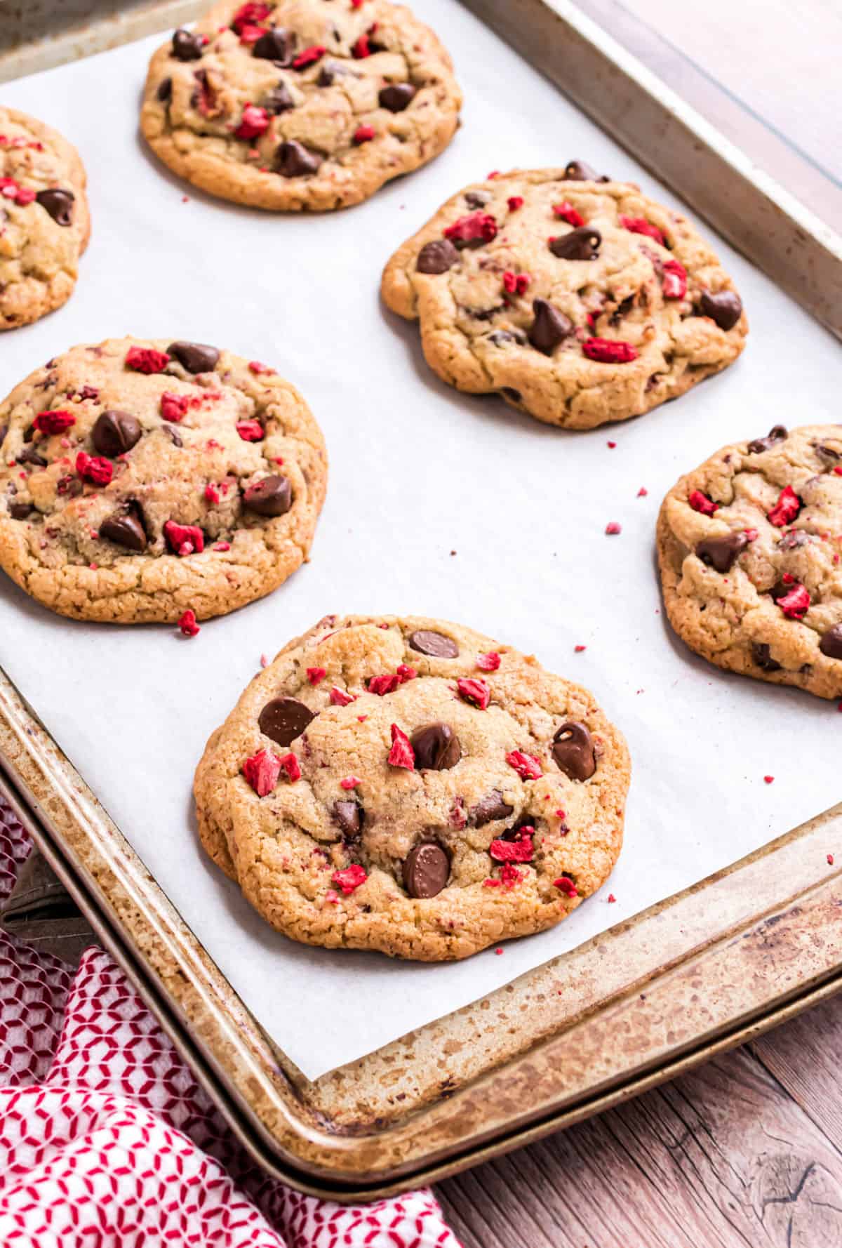 Chocolate chip cookies with strawberry pieces on parchment paper lined cookie sheet.