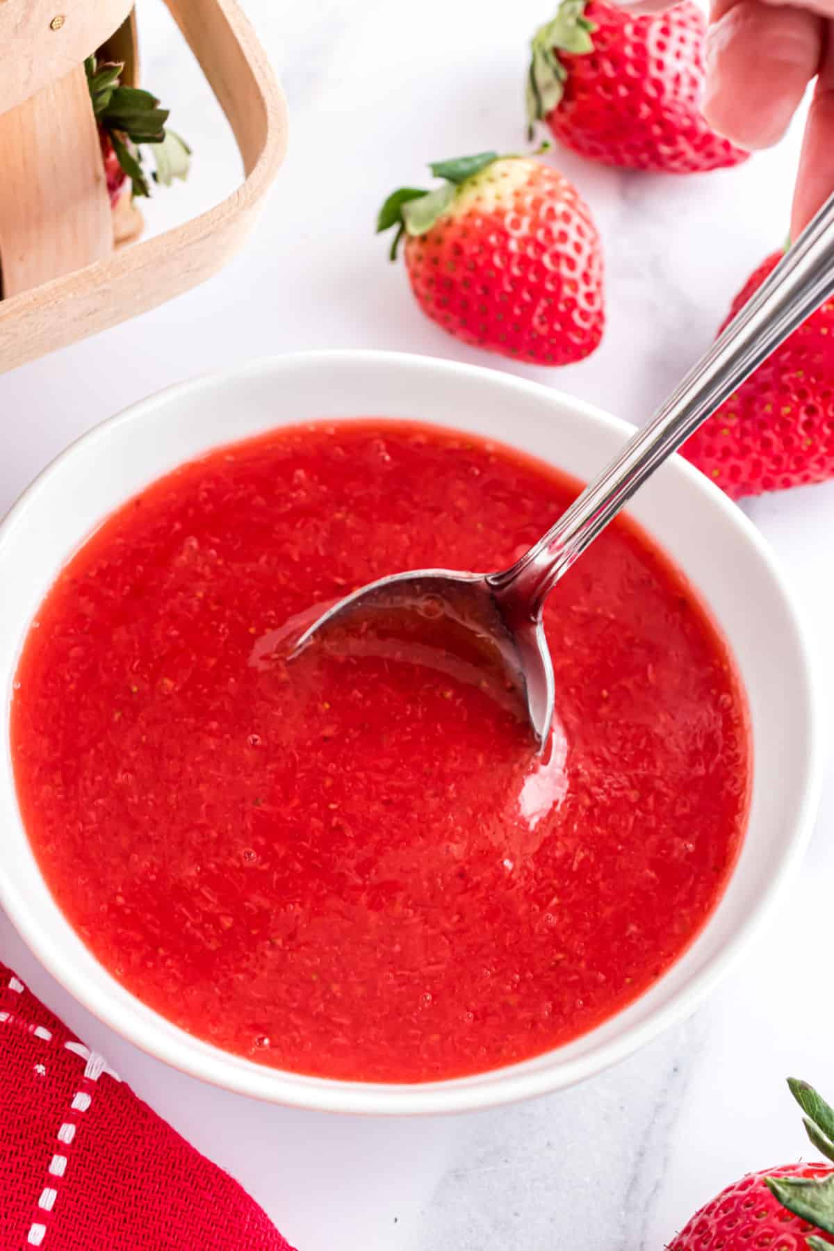 Strawberry syrup in a white bowl with spoon.