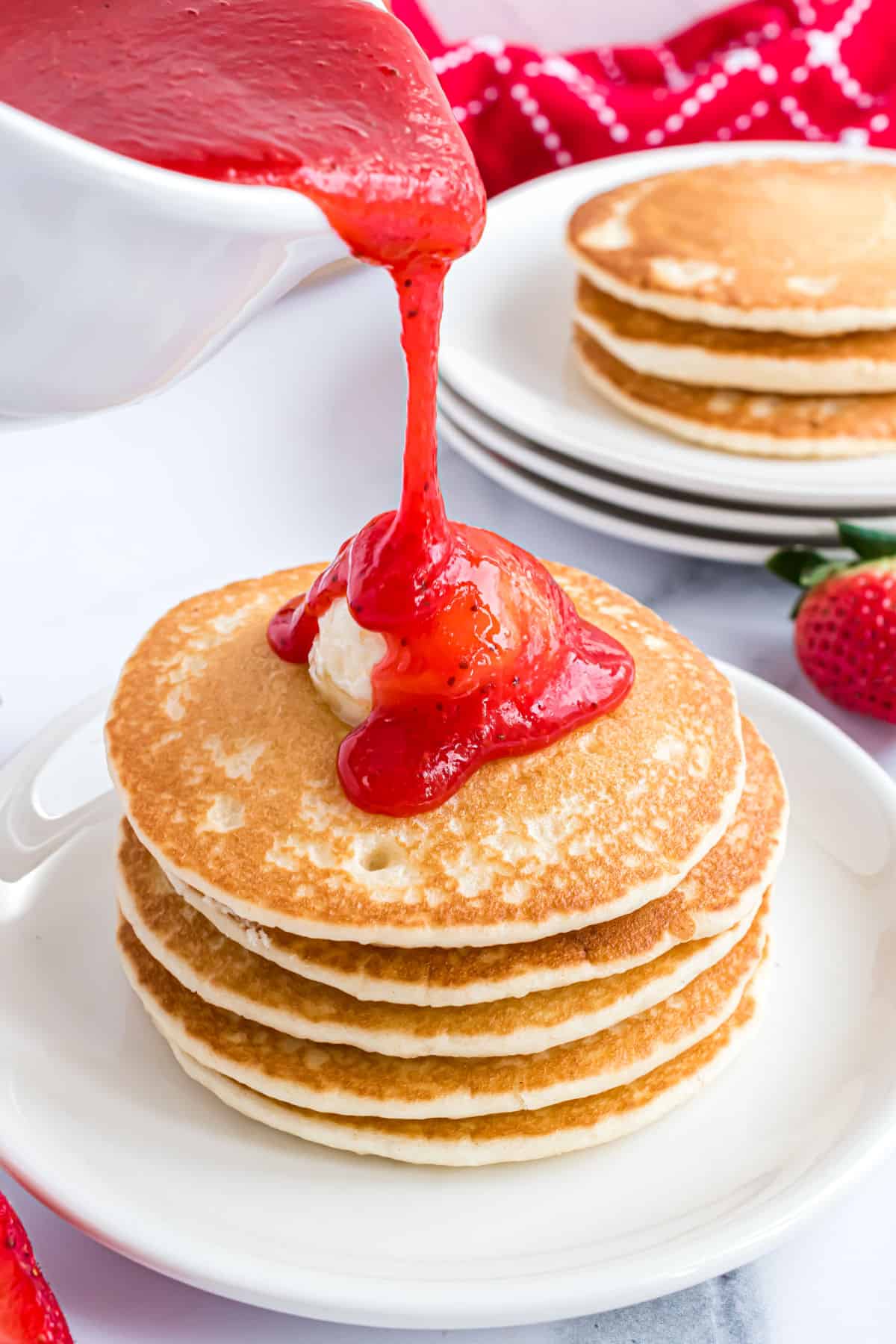 Pancakes with strawberry syrup being poured over top.