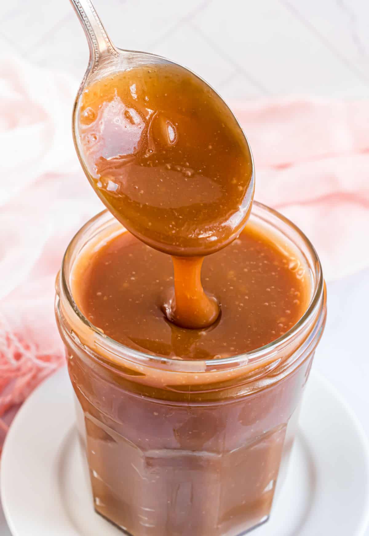 Caramel sauce in a glass jar with a spoon.