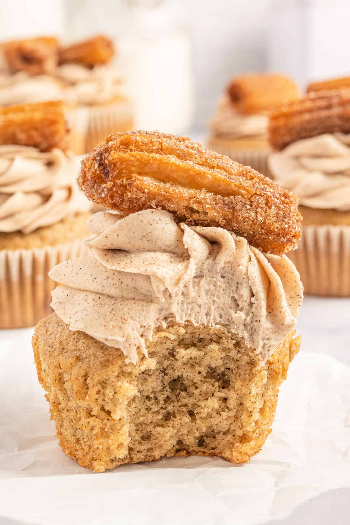 Cinnamon cupcake with churro on top and a bite taken out.