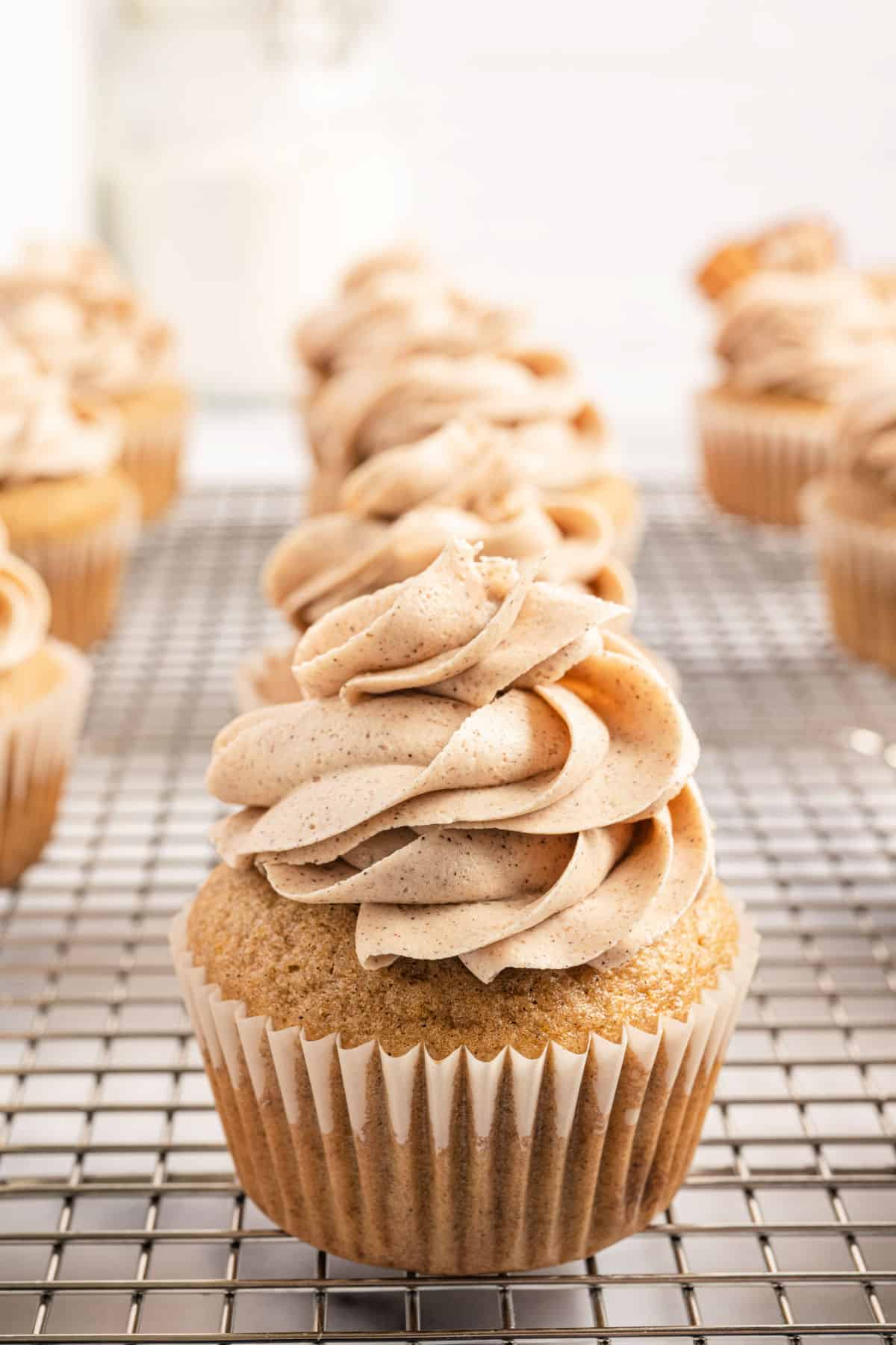 Cinnamon cupcakes on wire cooling rack topped with cinnamon frosting.