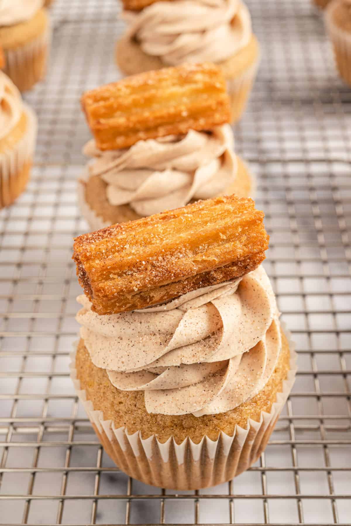 Cinnamon sugar frosted cupcake with a churro on top.