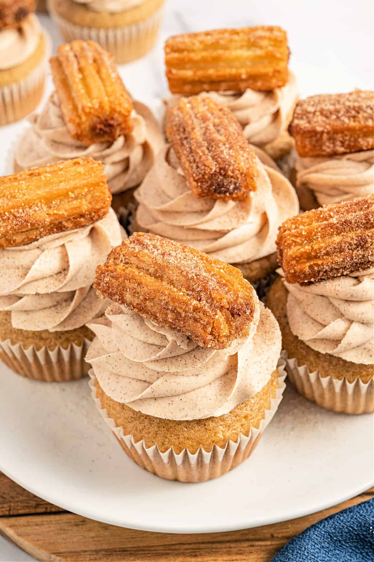 Churro topped cupcakes on a white serving platter.