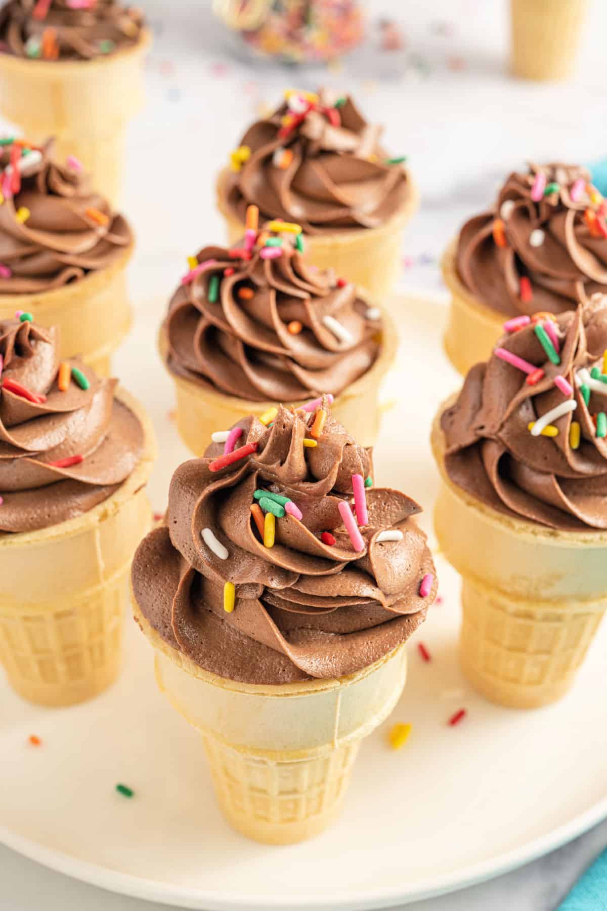 Ice cream cone cupcakes with chocolate frosting on a white serving plate.