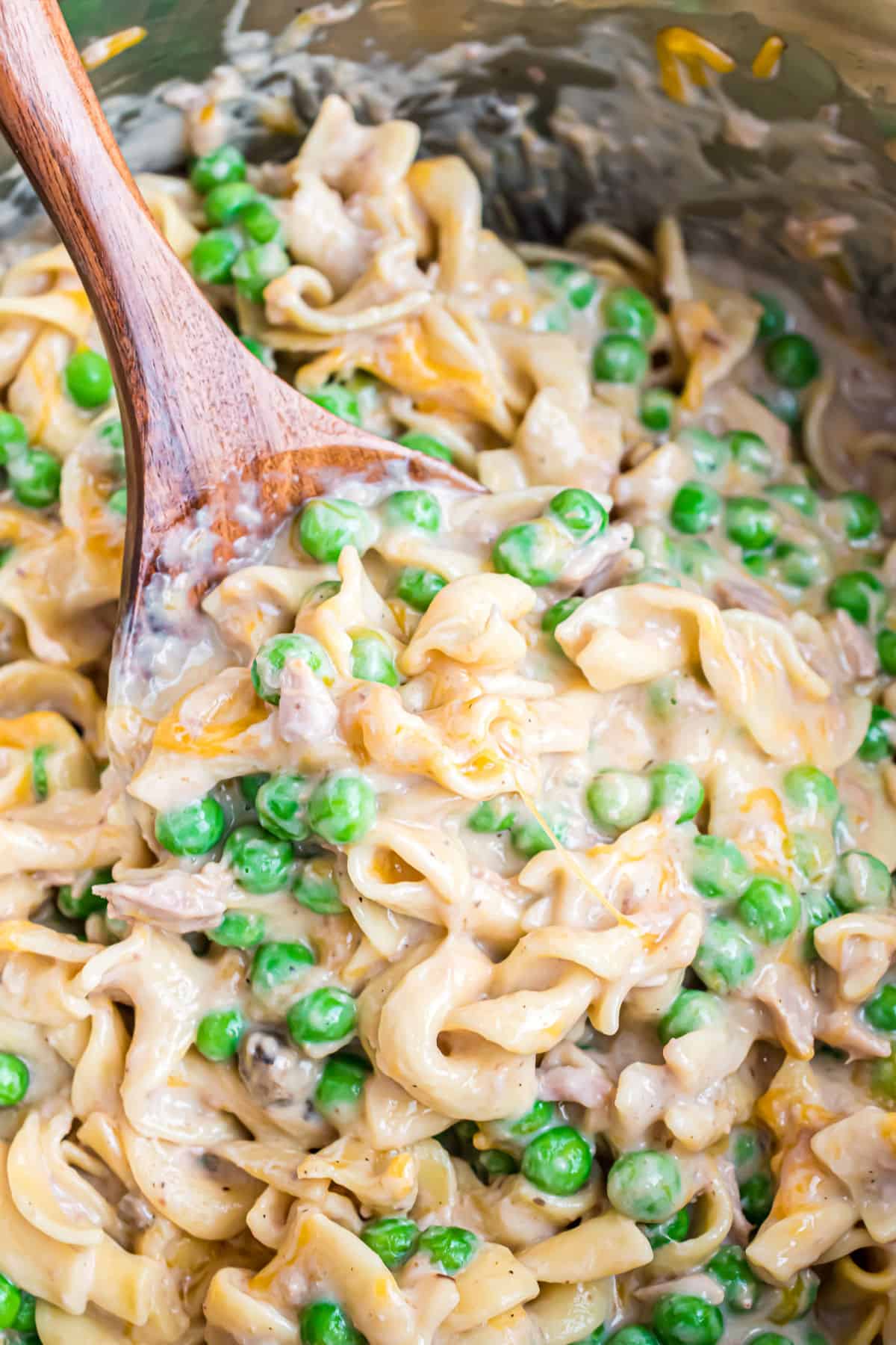 Tuna noodle casserole with peas being stirred with wooden spoon.