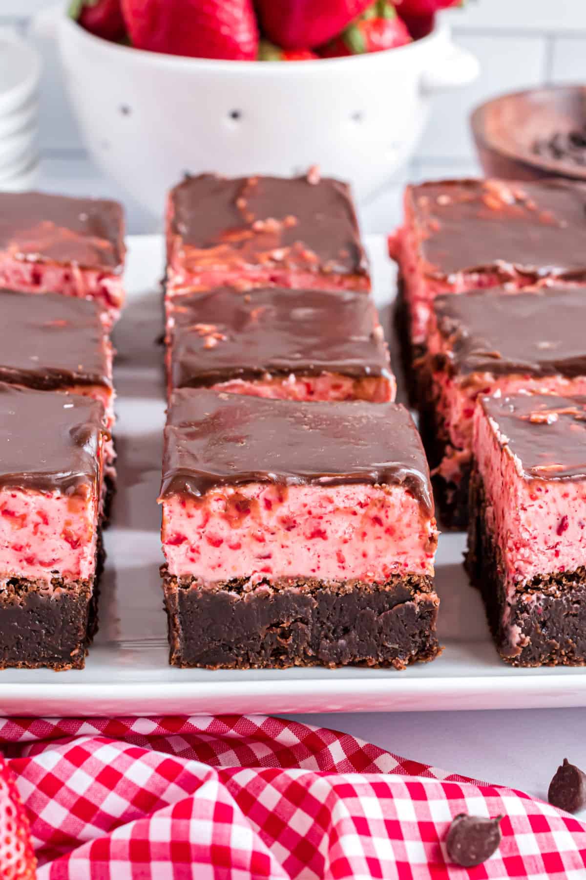 Brownies with strawberry frosting cut into squares on a white plate.