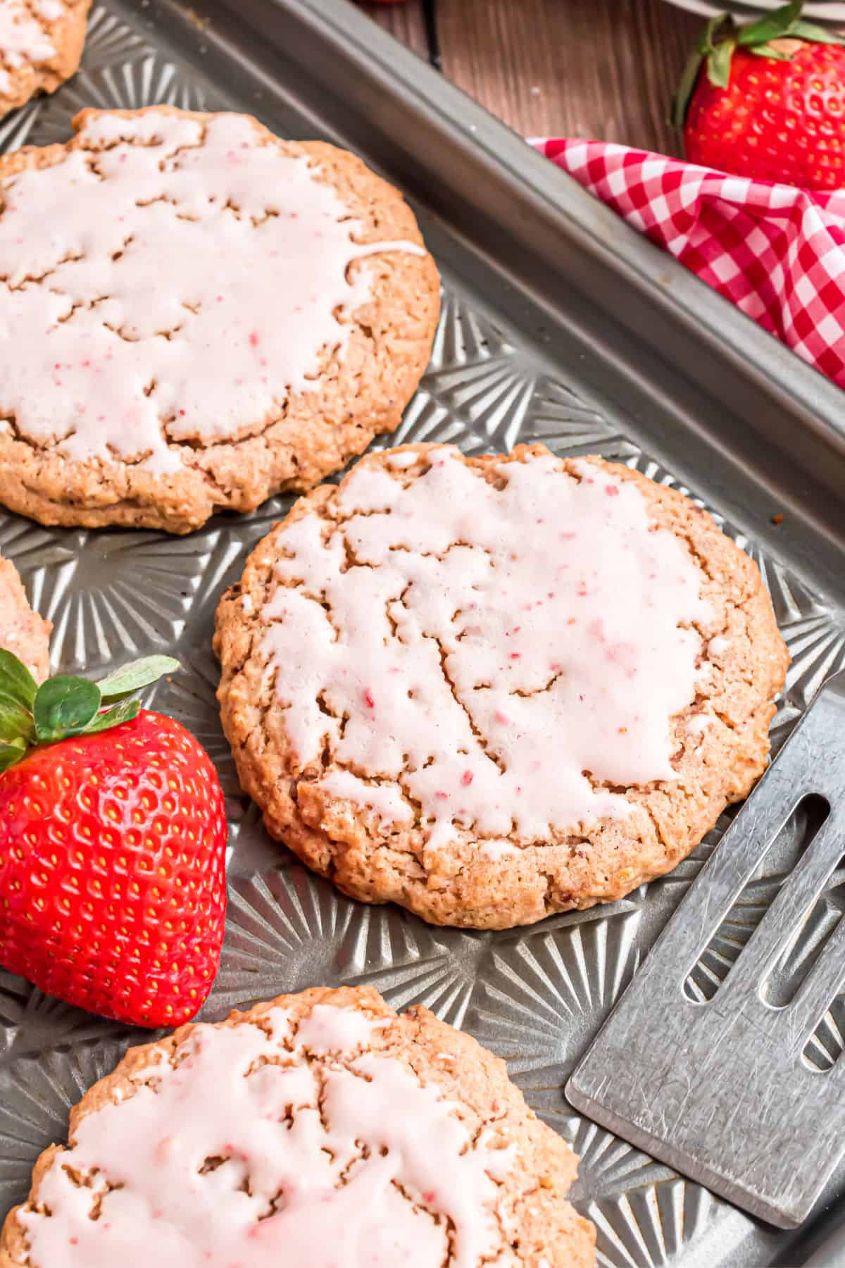Iced strawberry cookies on a baking sheet.