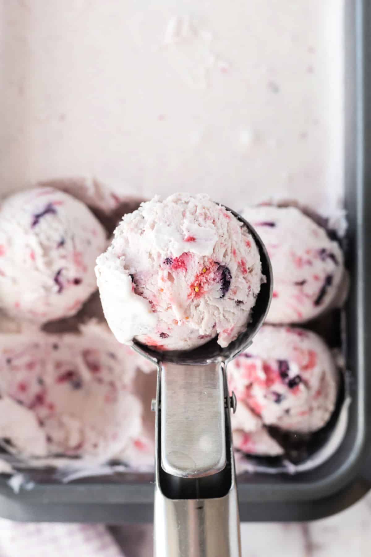 Berry ice cream being scooped out of metal dish.