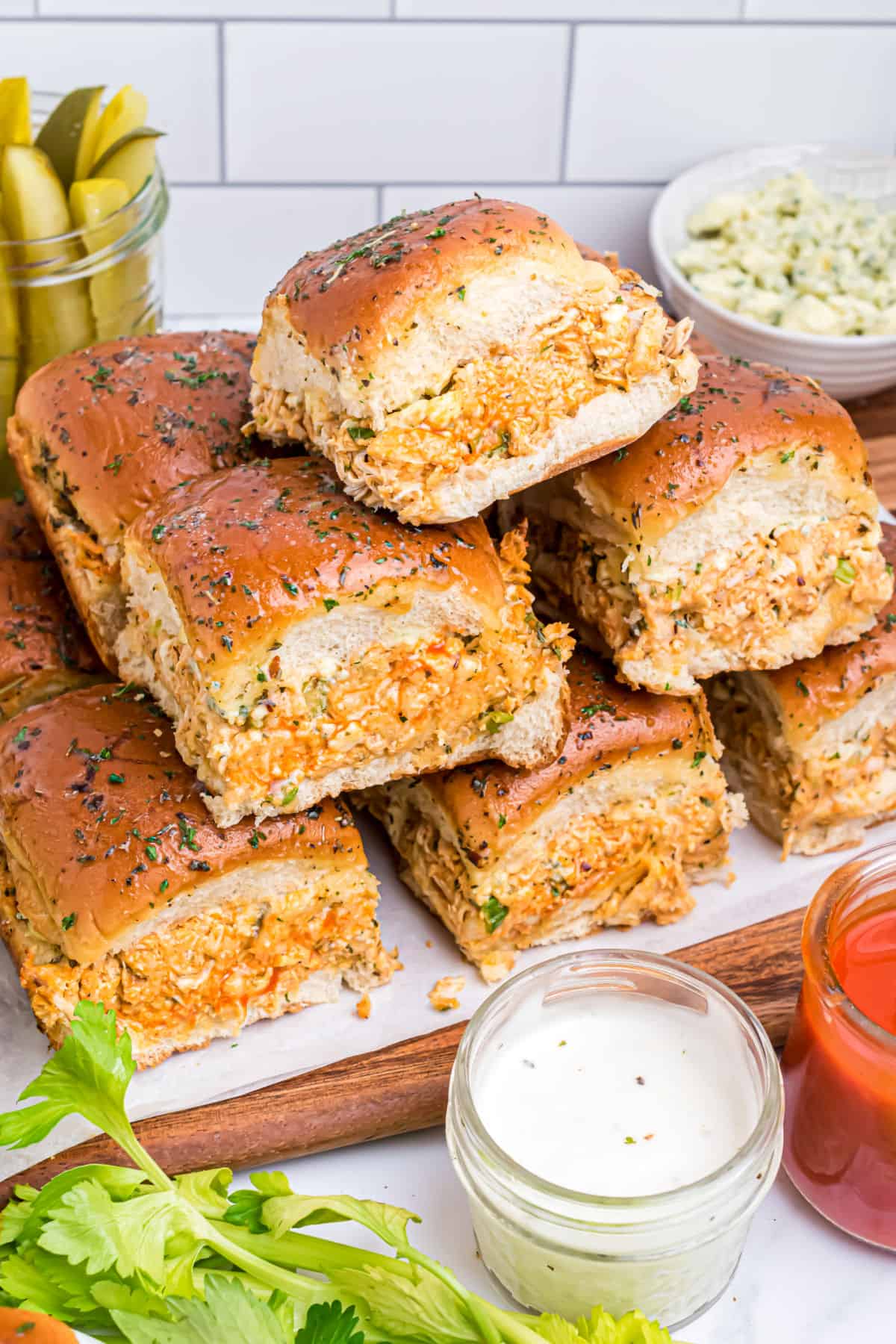 Stack of buffalo chicken sliders on a white plate with side of blue cheese dressing.