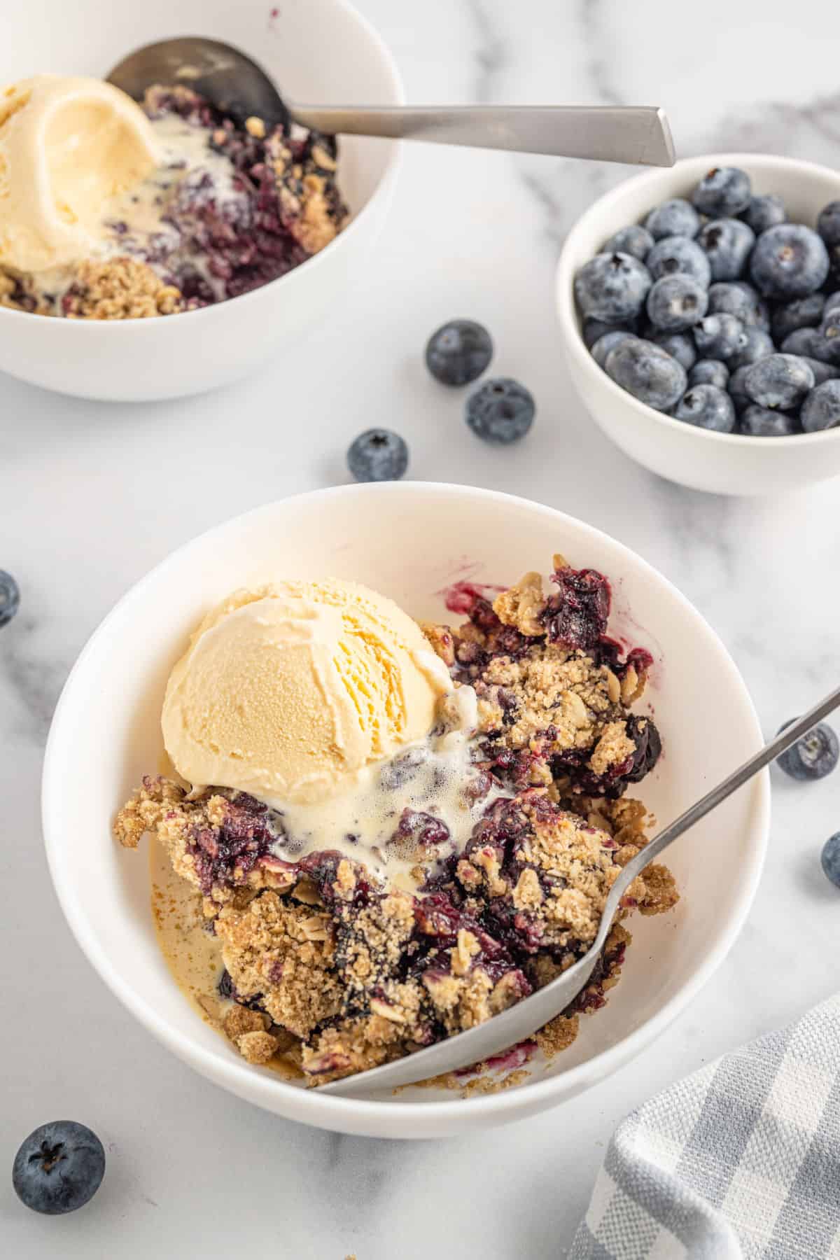 Blueberry crisp served in a white bowl with vanilla ice cream.