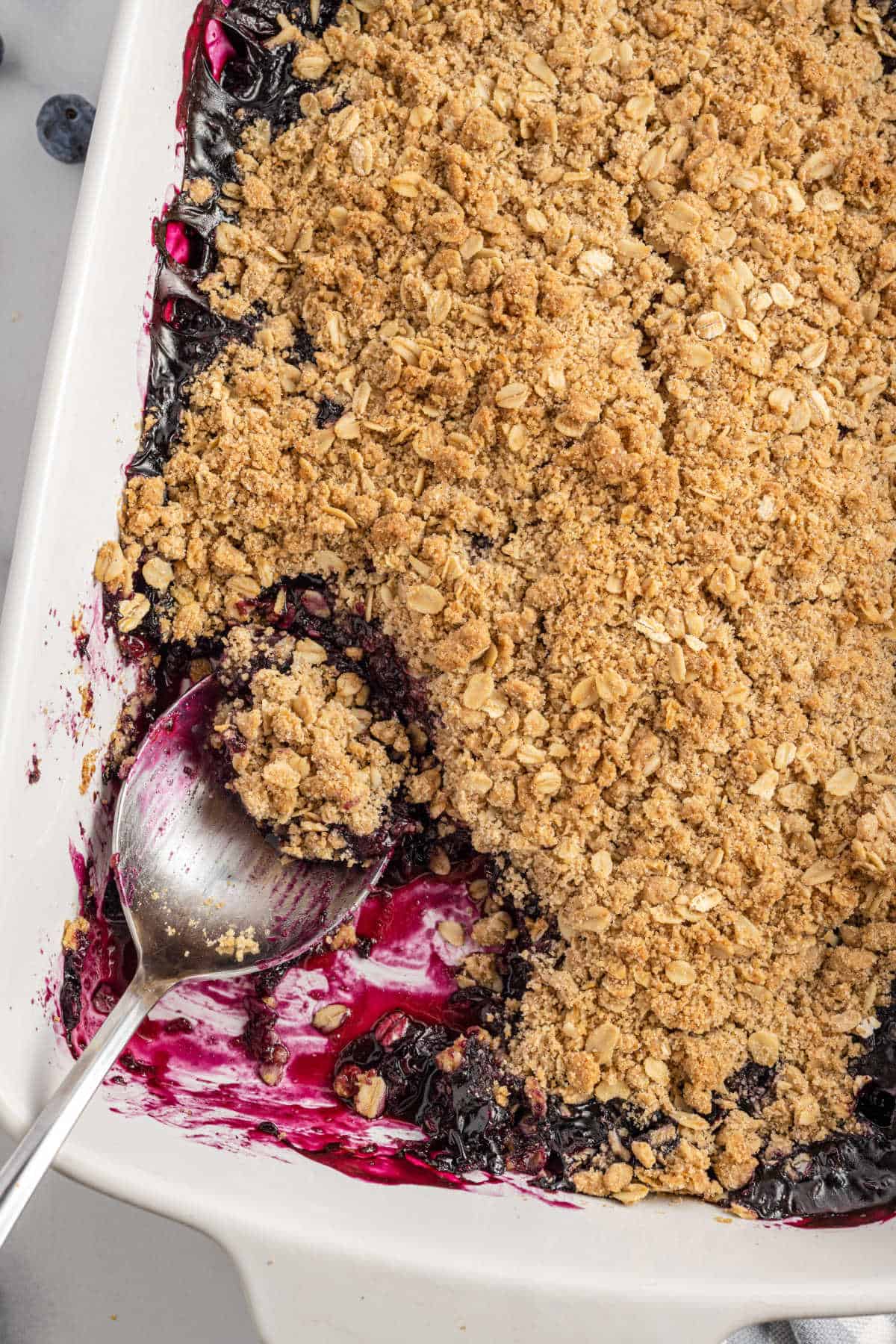 Blueberry crisp with oat topping in a 13x9 white baking dish with a spoon.