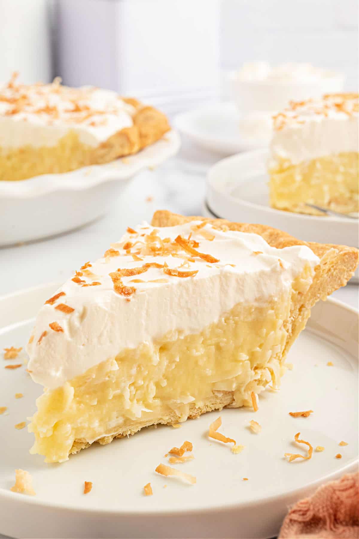 Slice of coconut cream pie on a white plate with toasted coconut.