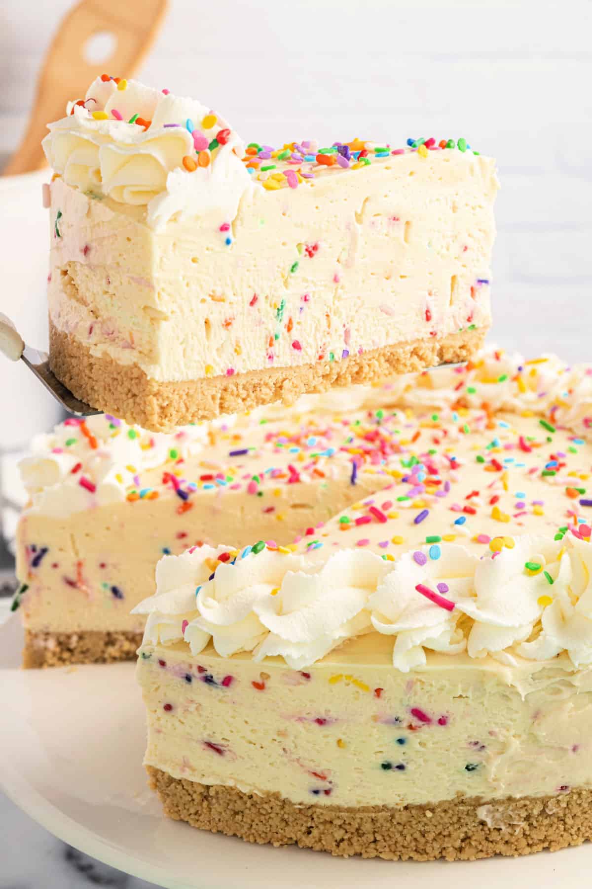Funfetti cheesecake slice being lifted off cake platter.