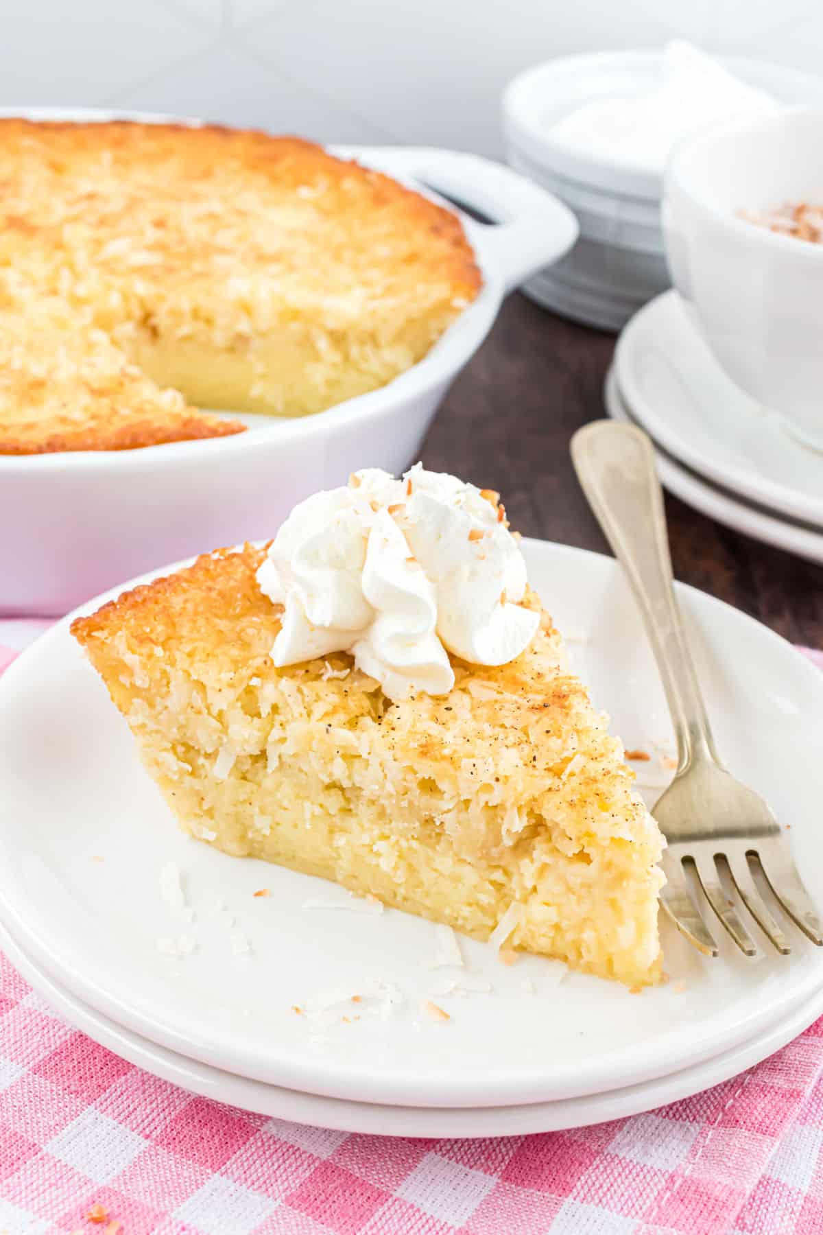 Slice of coconut pie on a white plate with a dollop of whipped cream.