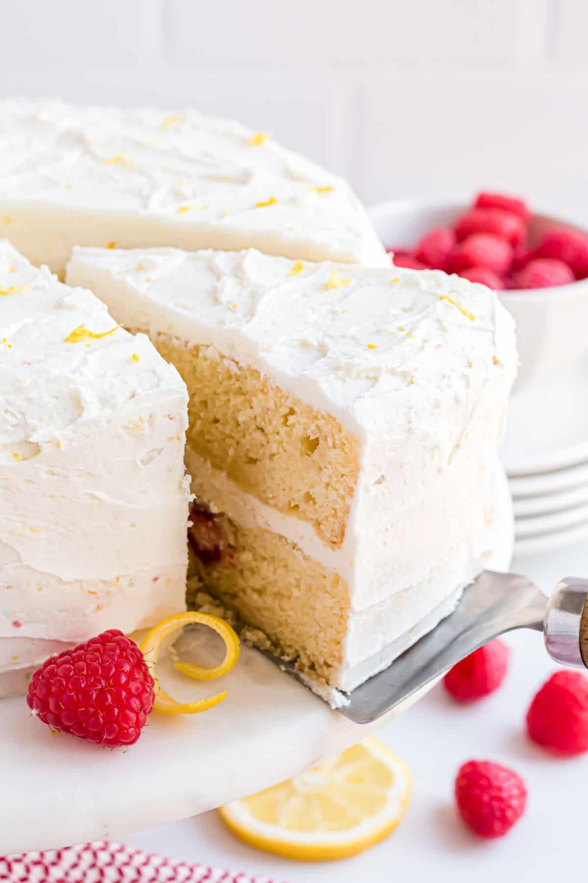 Raspberry lemon layer cake with a cut slice being removed from cake platter.