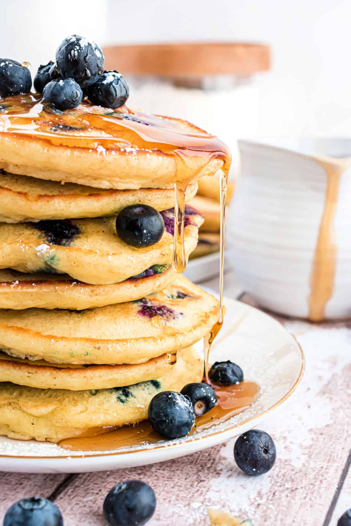 Blueberry pancakes stack on a plate with syrup dripping off.