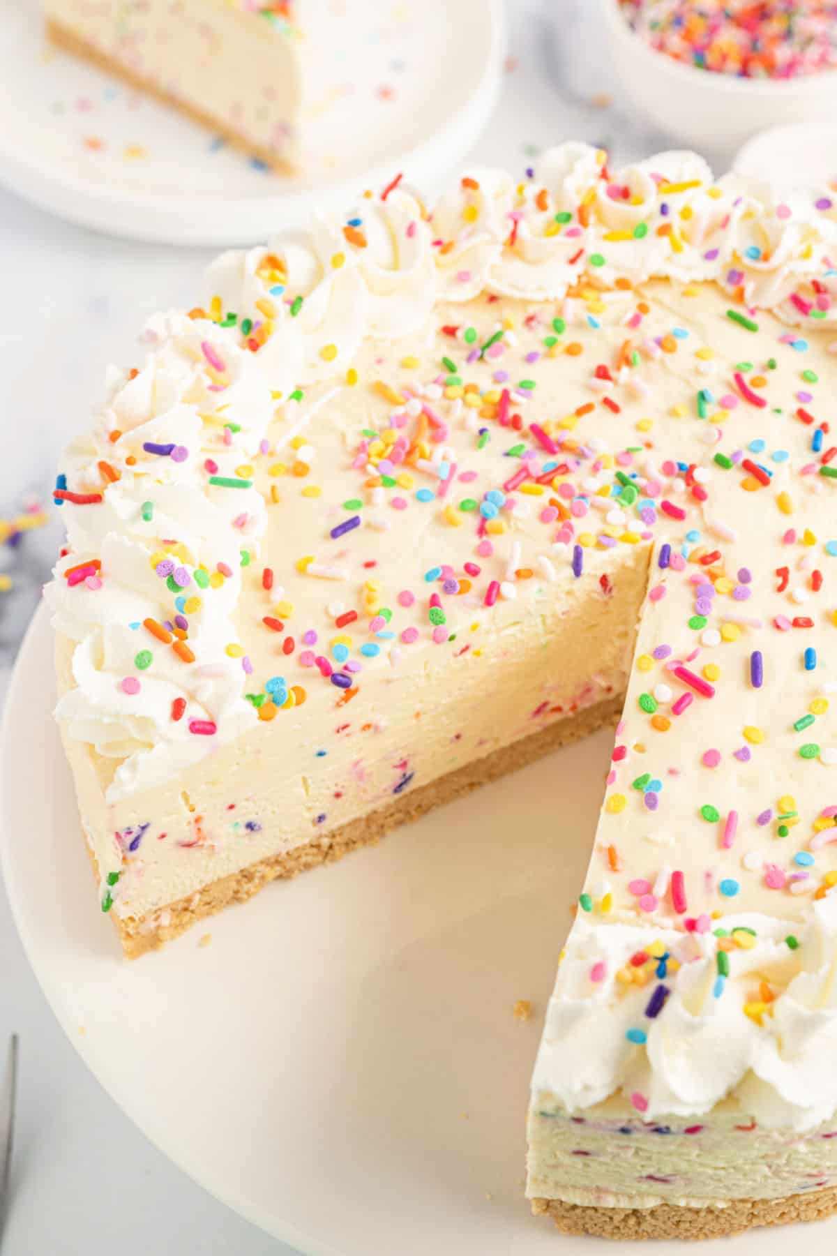 Cheesecake with sprinkles and slice removed from cake platter.