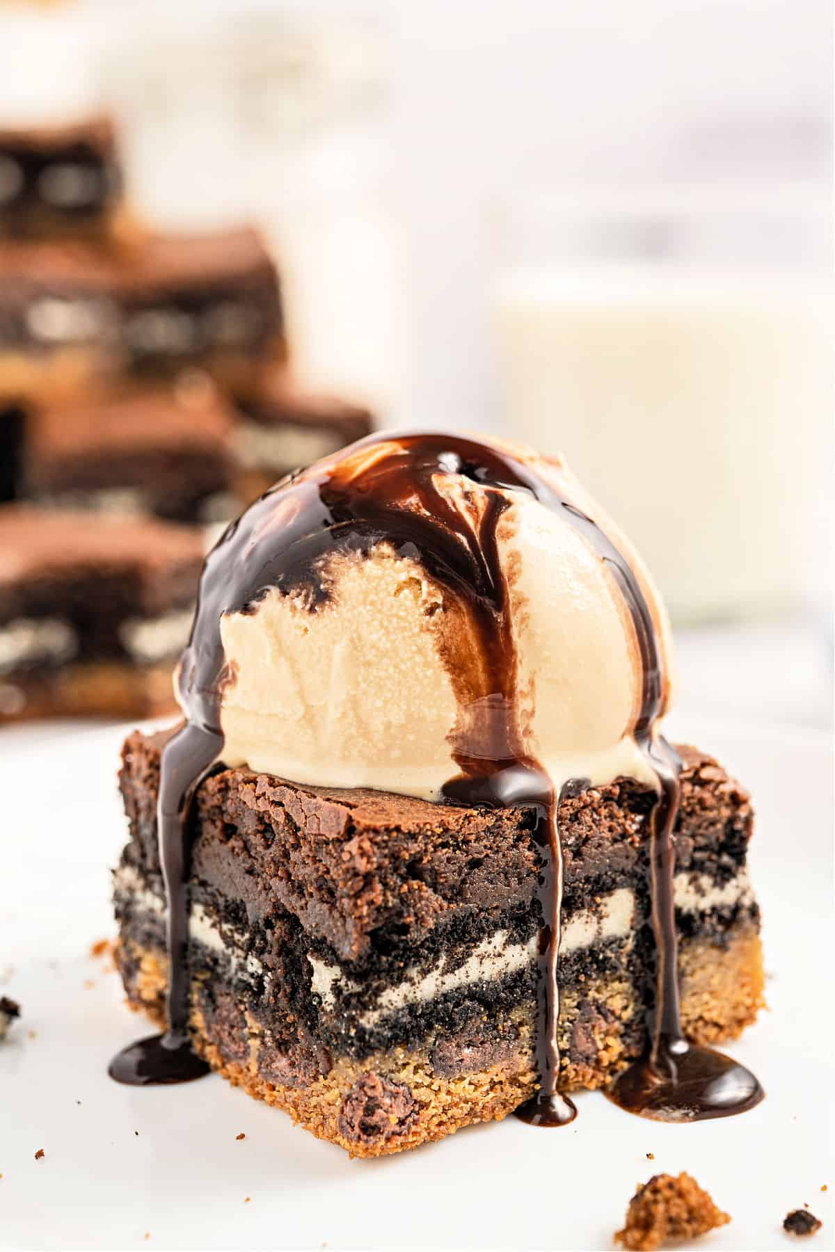 Layered dessert of cookie, oreo, and brownies topped with ice cream and hot fudge.