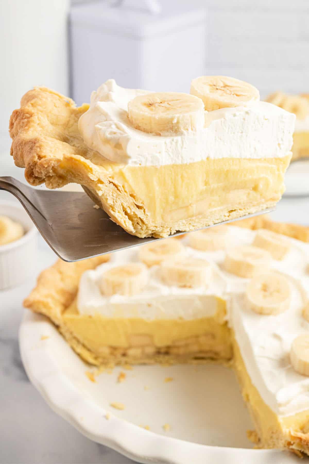 Banana cream pie with a slice being removed with a pie spatula.