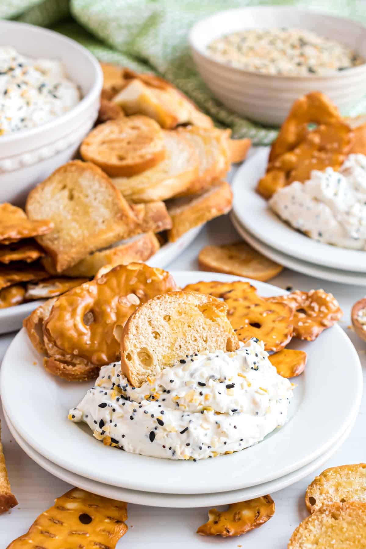 Everything bagel dip served on a white plate with pretzels and bagel chips.