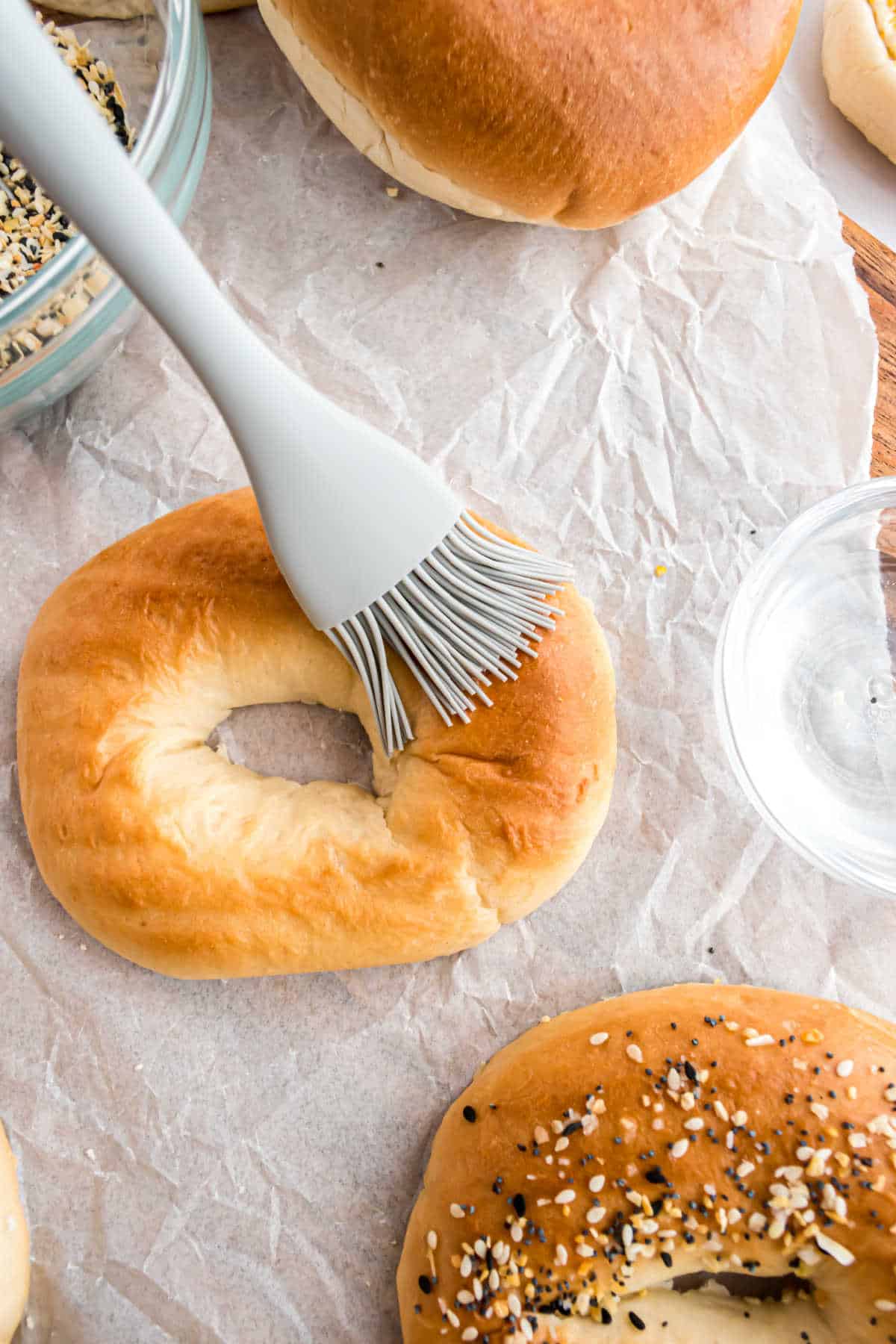 Pastry brush on a bagel with seasoning mix in a bowl.