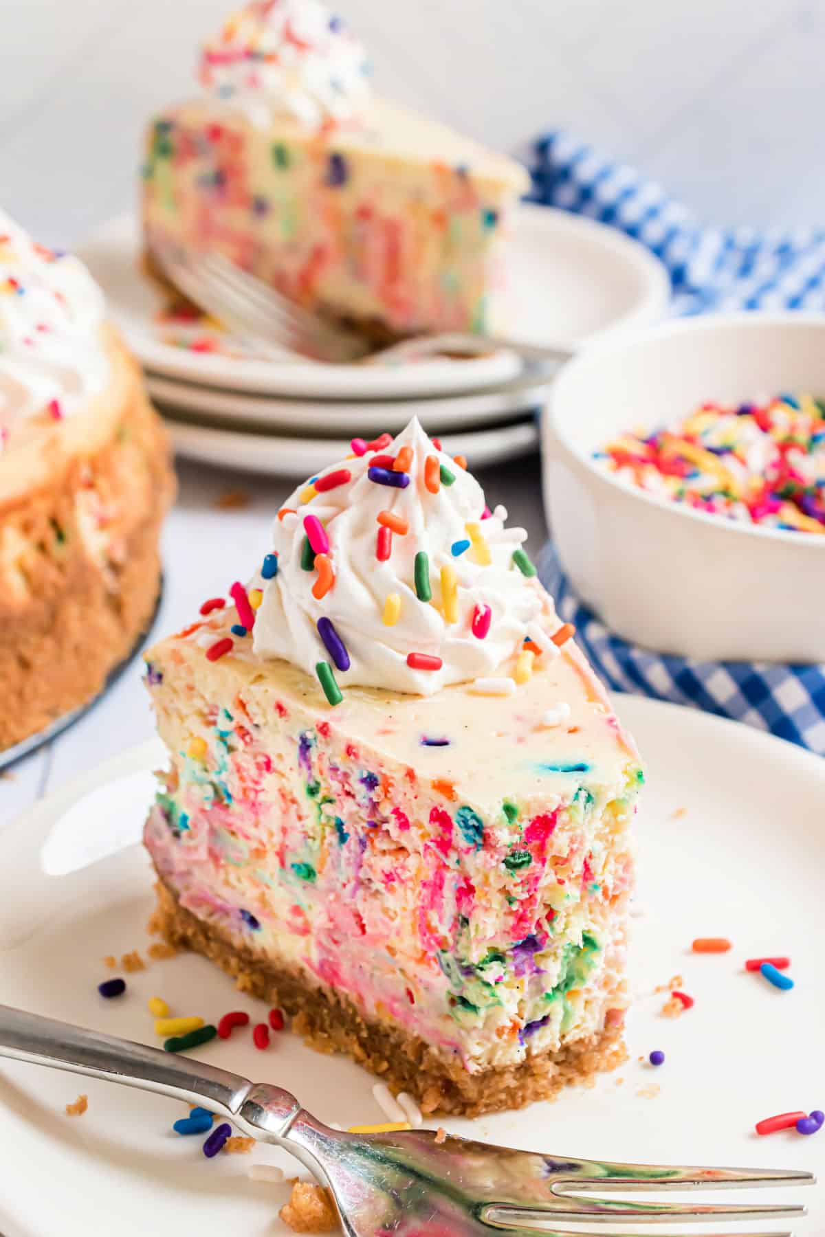 Slice of cheesecake with sprinkles on a plate with a bite removed.