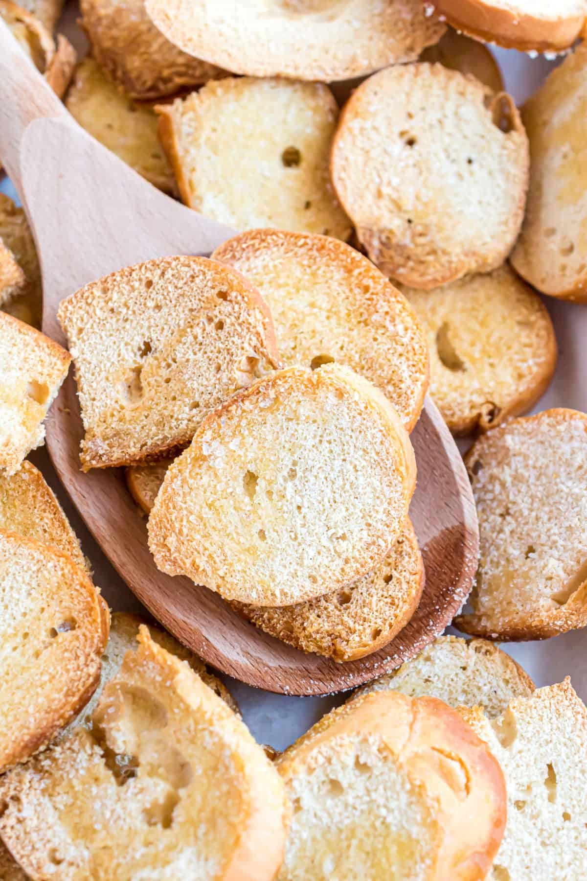 Baked bagel chips being scooped off cookie sheet.