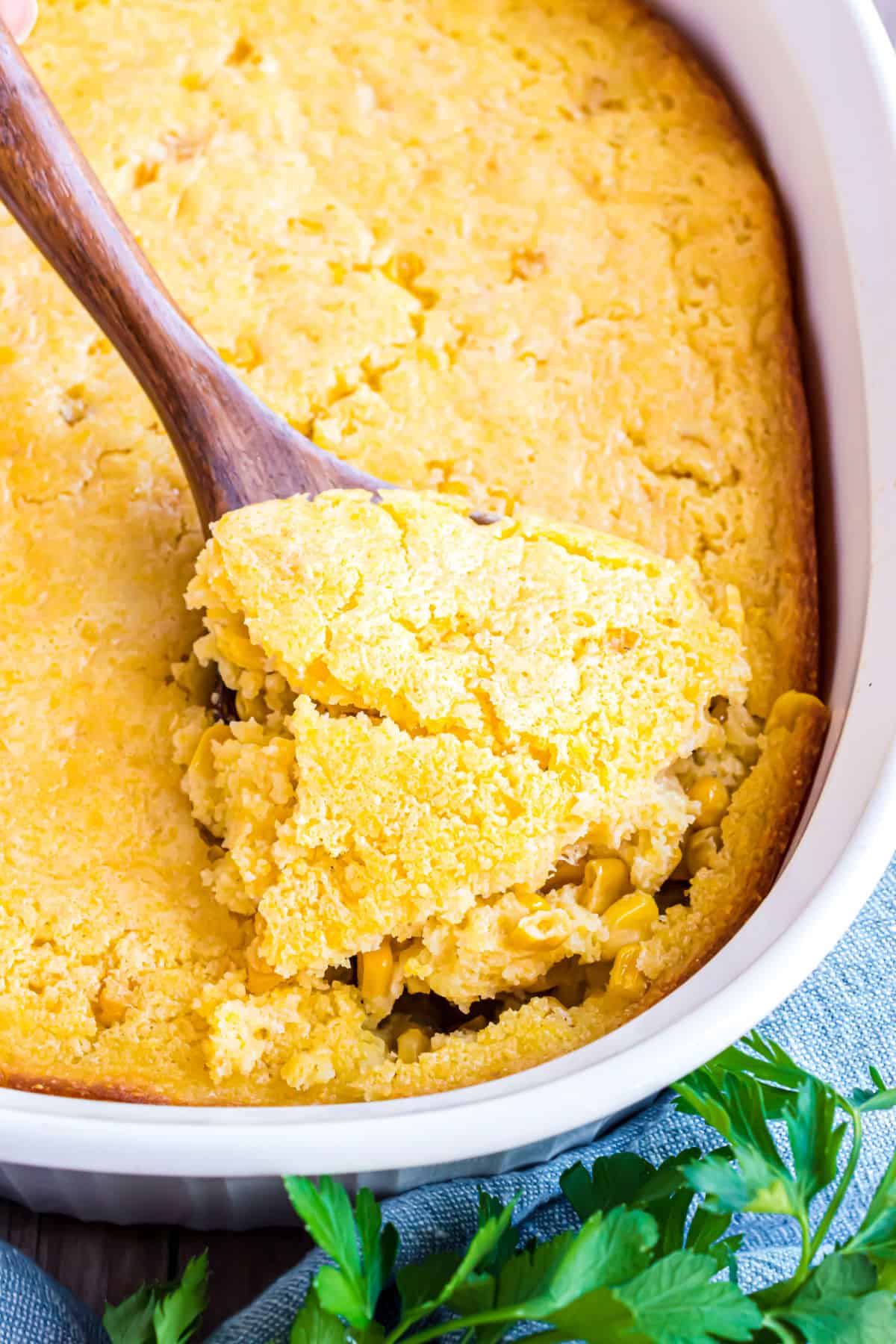 Corn casserole baked in a white baking dish with a spoon serving it up.