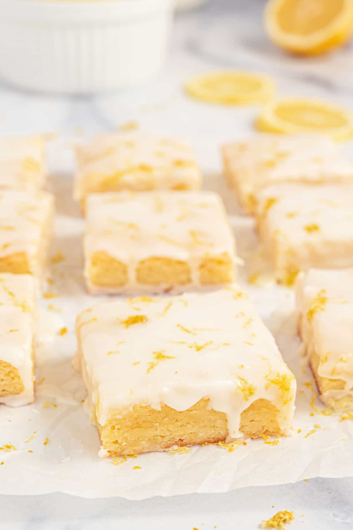 Lemon brownies with icing cut into squares on parchment paper.