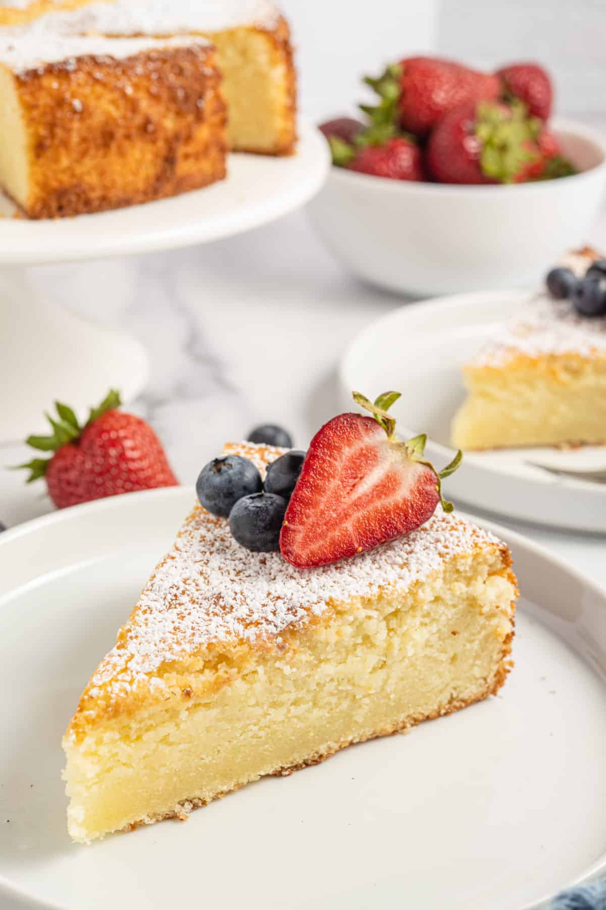 Slice of lemon ricotta cake topped with powdered sugar and berries.