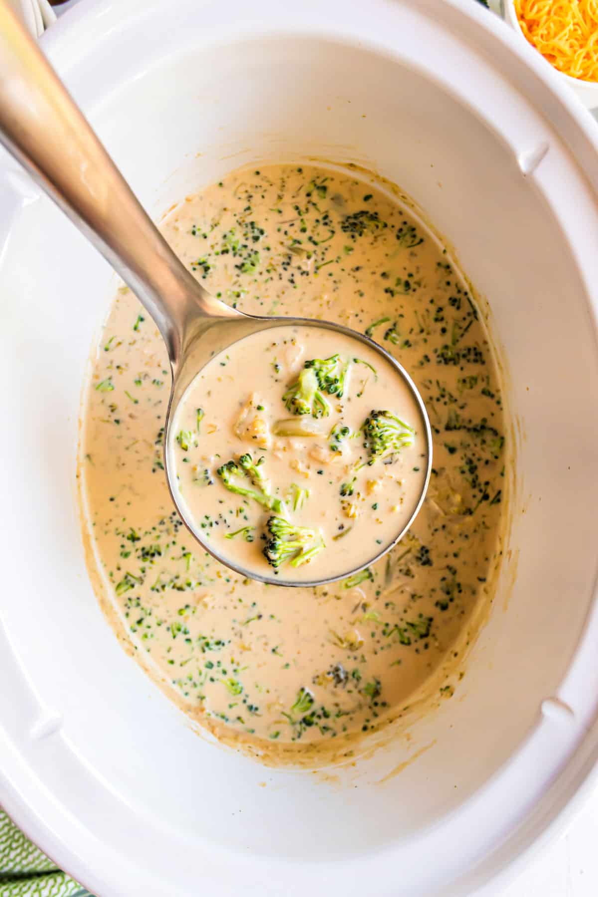 Broccoli cheese soup in a white slow cooker with a ladle.