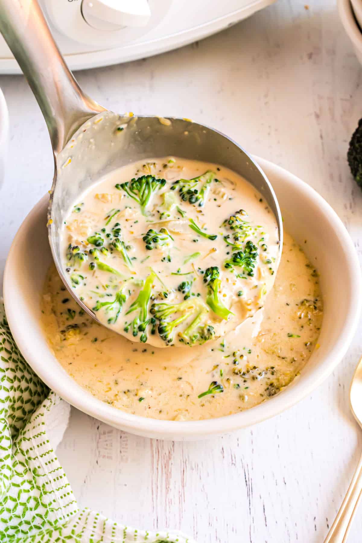 White bowl with broccoli cheese soup being ladled into it.