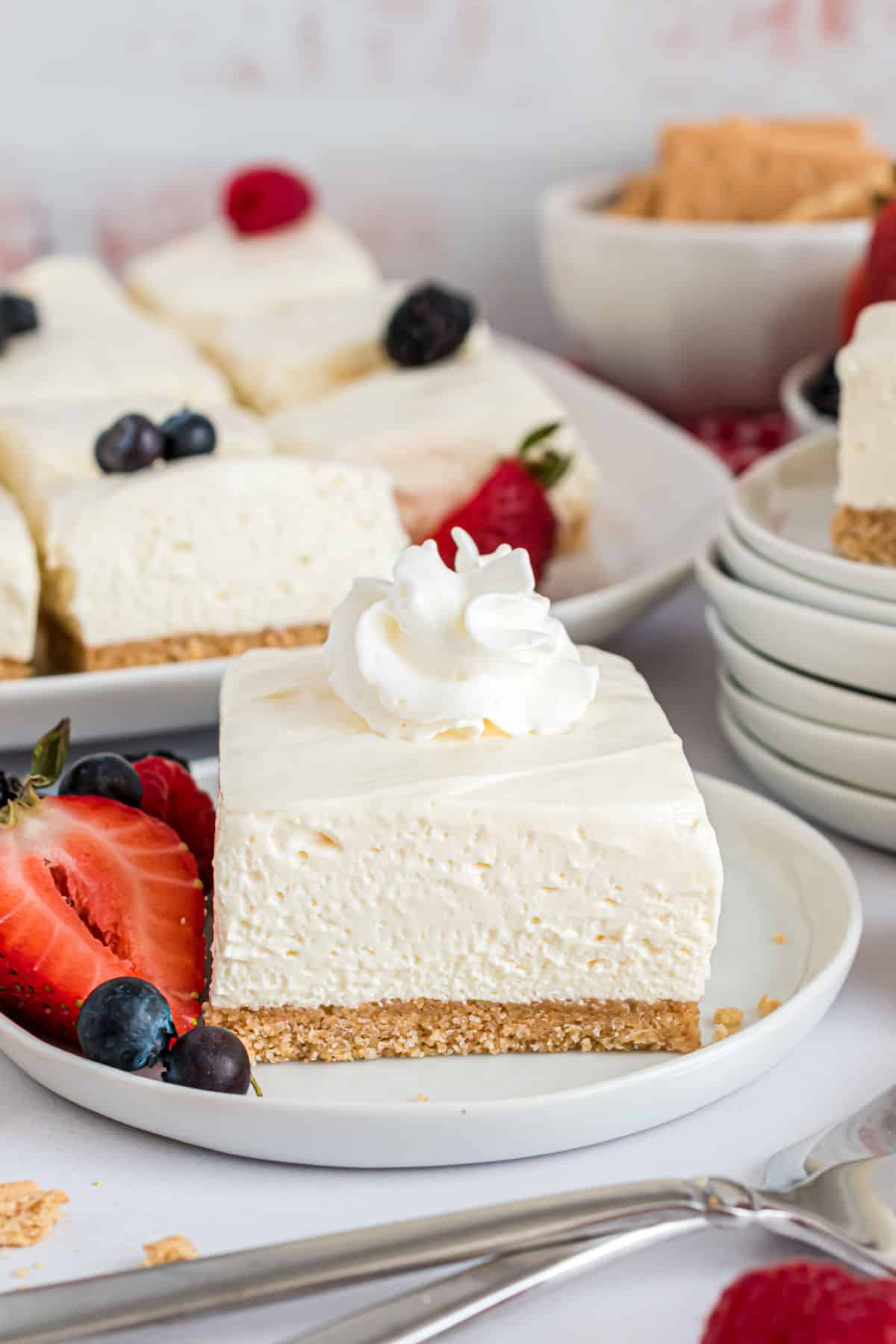 Slice of no bake cheesecake bar topped with whipped cream.