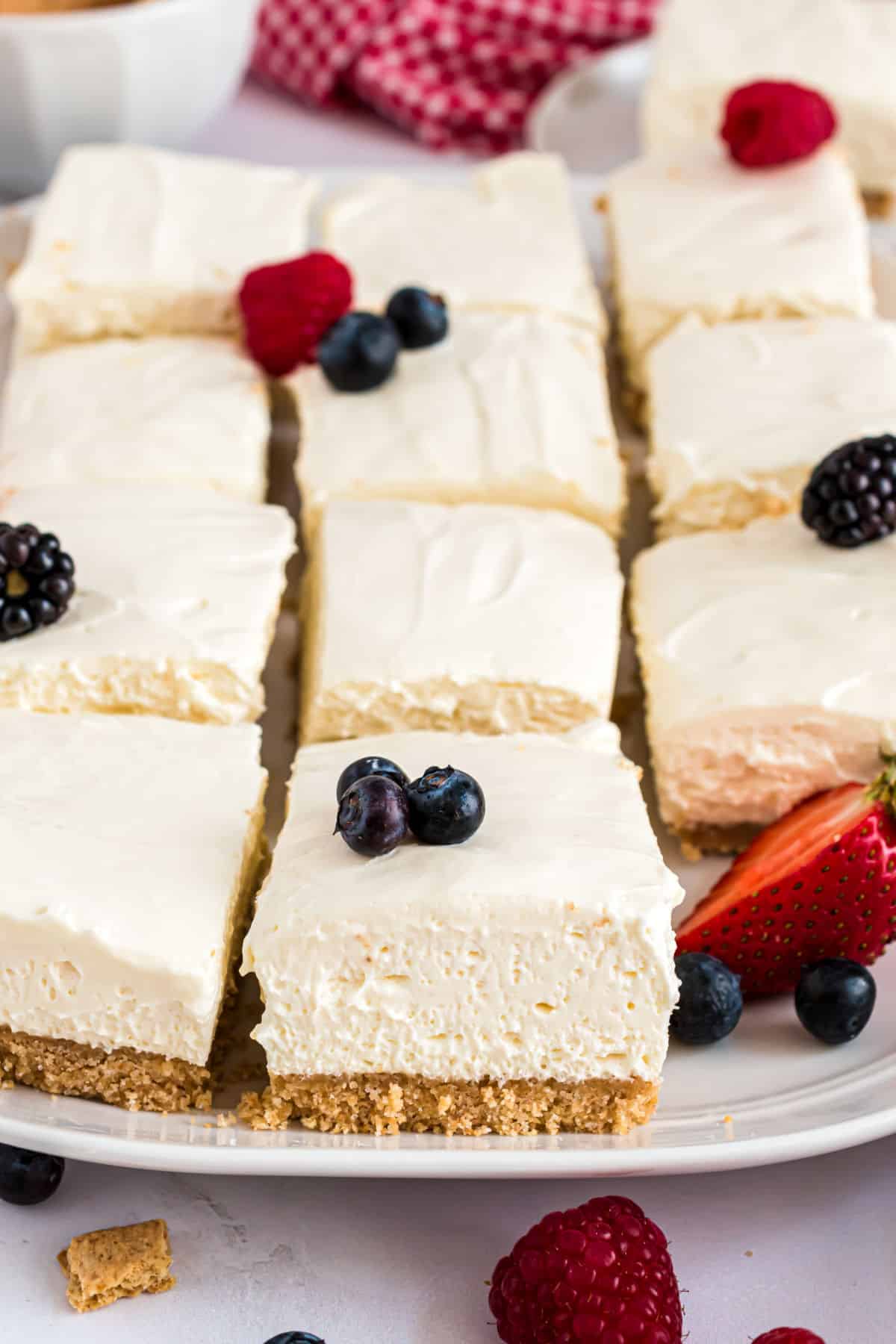 Large serving plate with cheesecake bars topped with fresh berries.