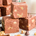 Three pieces of chocolate walnut fudge stacked on parchment paper.