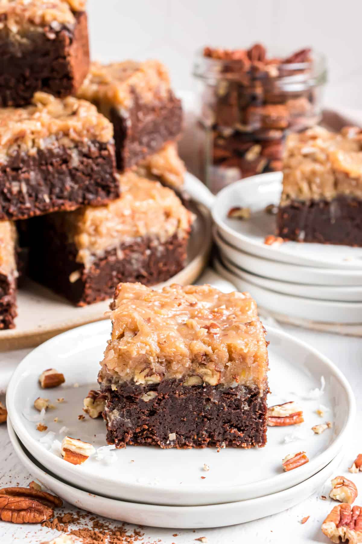 Slice of german chocolate brownie served on a stack of white plates.