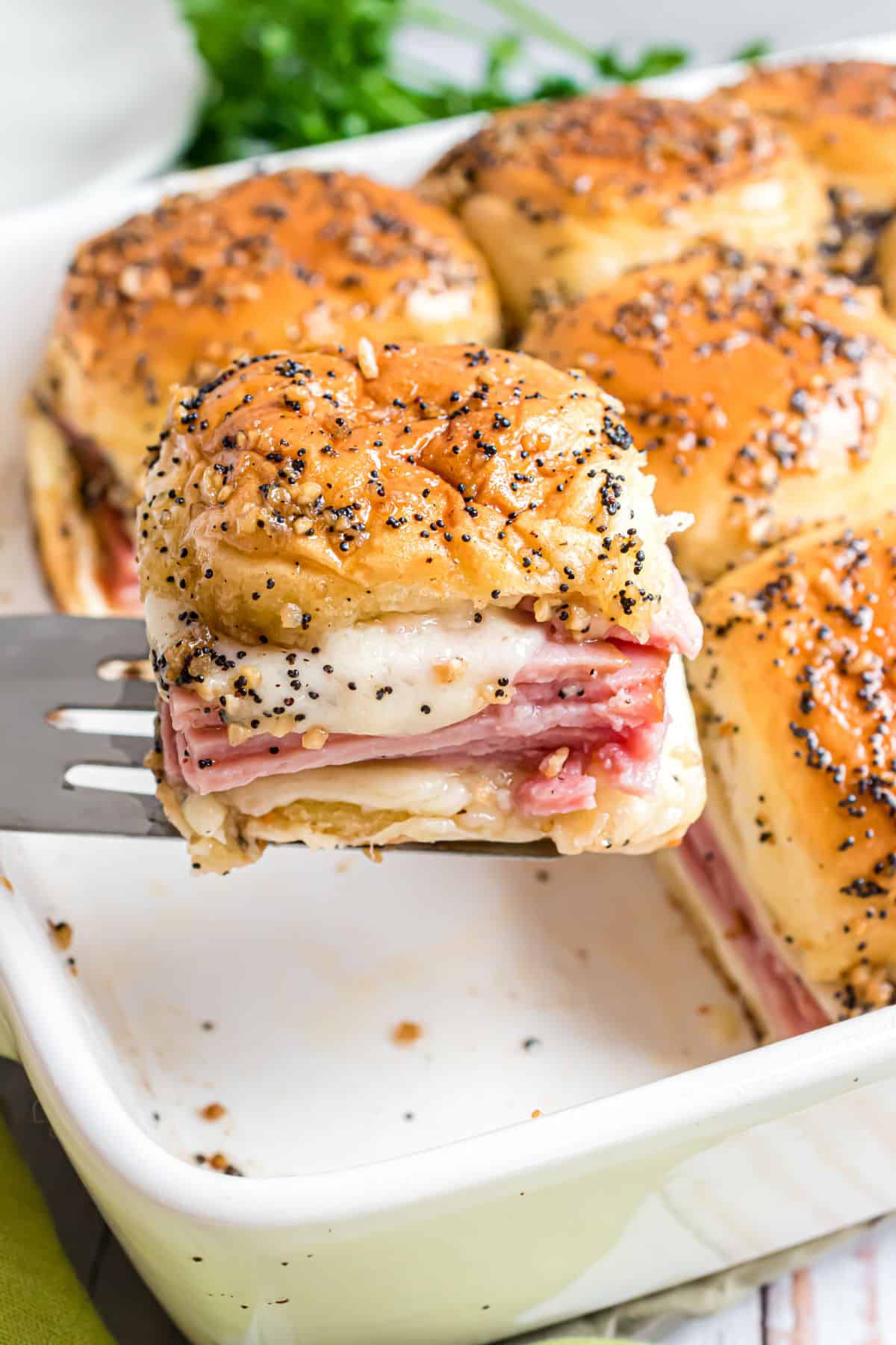 Ham and cheese sliders being lifted out of white baking dish.