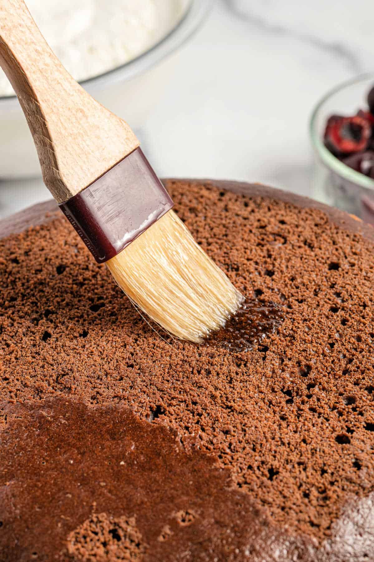 Cherry syrup being brushed onto baked cake.