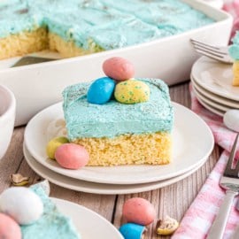 Slice of yellow cake and blue frosting on a white plate.