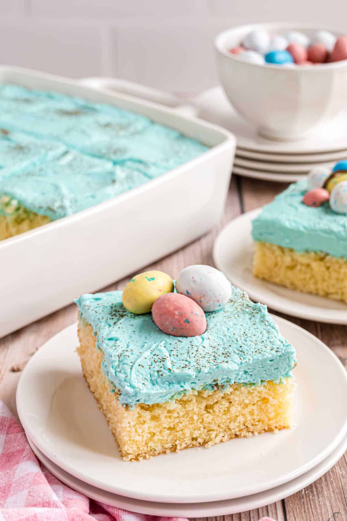 Slice of cake with light blue frosting and Robins eggs served on a stack of white plates.