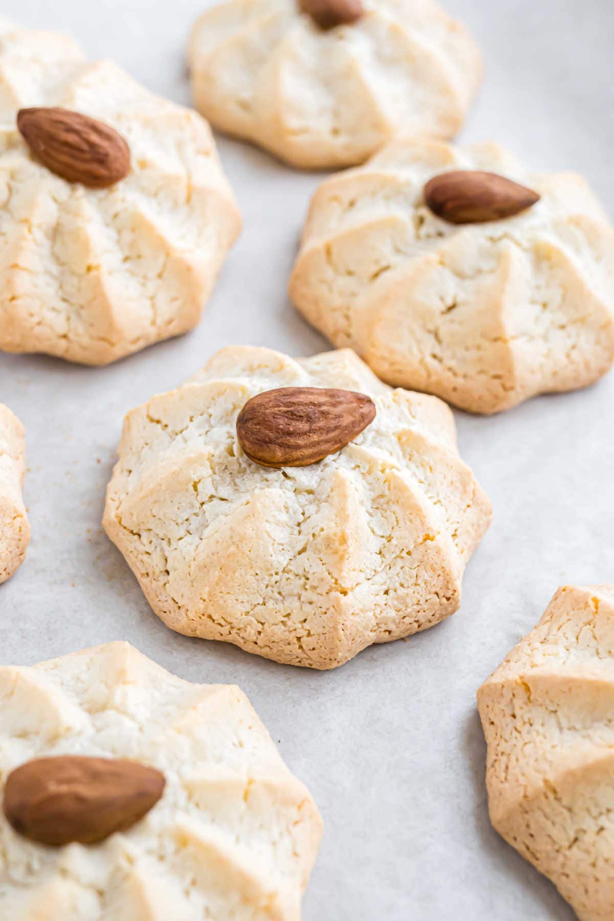 Almond cookies with cracked tops, reminiscent of classic amaretti cookies, each topped with a whole almond and arranged on a light surface.