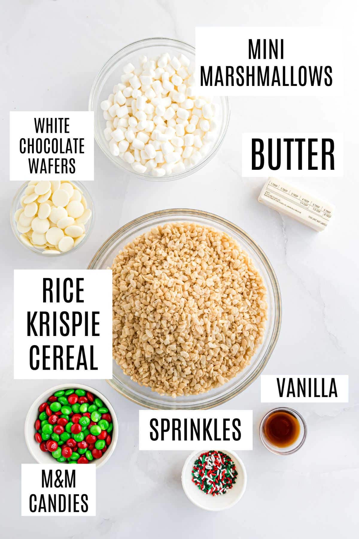 Bowls of Rice Krispie cereal, mini marshmallows, white chocolate wafers, butter, vanilla, sprinkles, and M&M candies—everything you need to make festive holiday Rice Krispie treats.