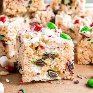A close-up of holiday Rice Krispie treats decorated with red, green, and white candies and bits of chocolate.