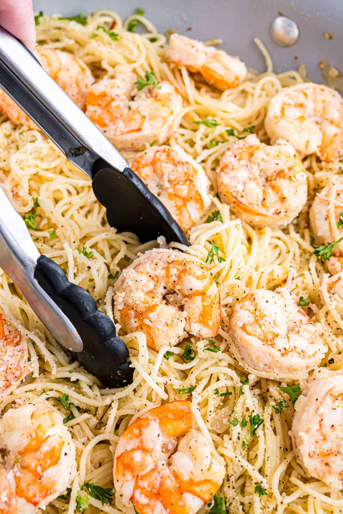 Tongs serving delicious shrimp scampi with angel hair pasta, garnished with fresh herbs and grated cheese.