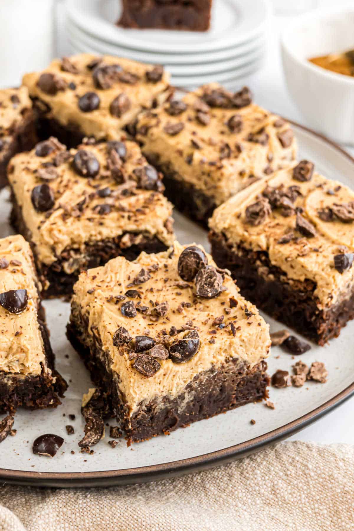 Espresso brownies topped with creamy frosting, chocolate shavings, and chocolate-covered coffee beans on a plate.